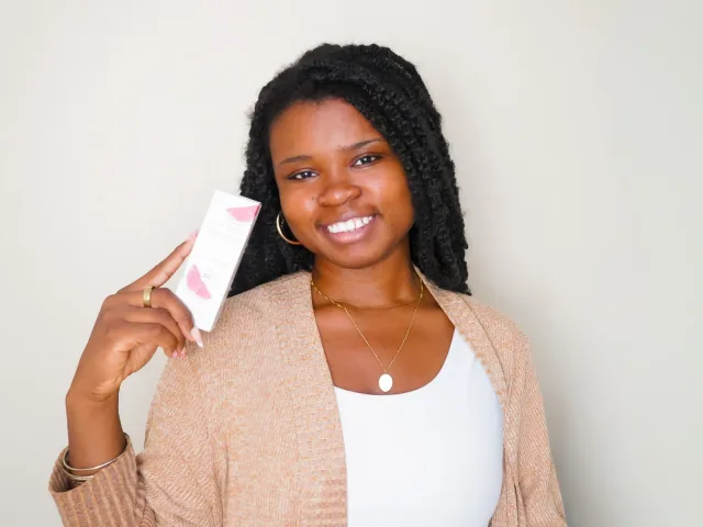 Faye presenting a pink skincare product with a natural smile
