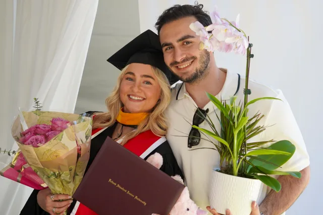 A graduate celebrating with a loved one and flowers
