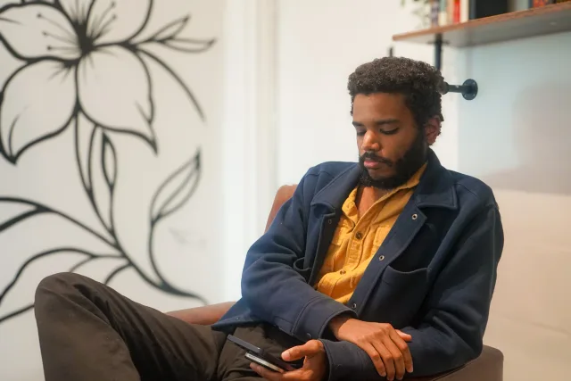 Isaiah Mallard seated beneath a botanical wall illustration at Drip Café