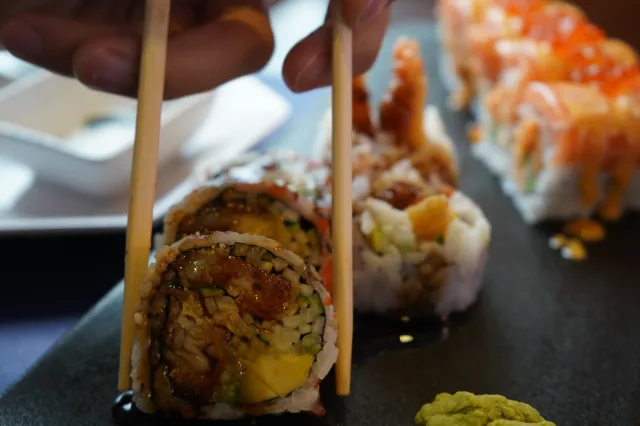 Chopsticks lifting a sushi roll from a serving board