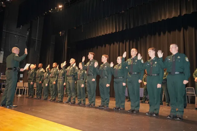 Graduates raising their right hands together on stage at a police graduation