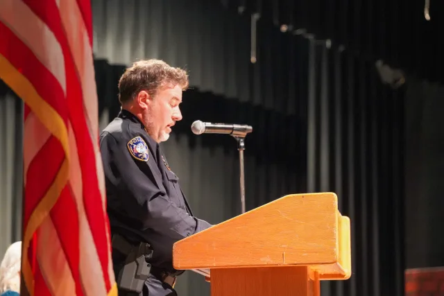 A uniformed speaker addressing the graduation ceremony at a microphone