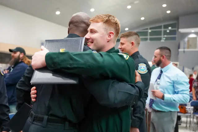 A smiling graduate sharing an embrace while holding his diploma