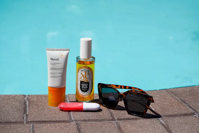 Sunscreen, body mist, lip care and sunglasses styled beside the pool
