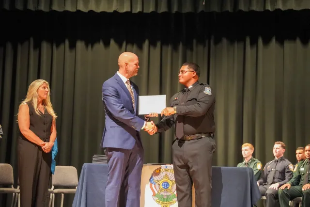A police graduate receiving a certificate with a handshake on stage